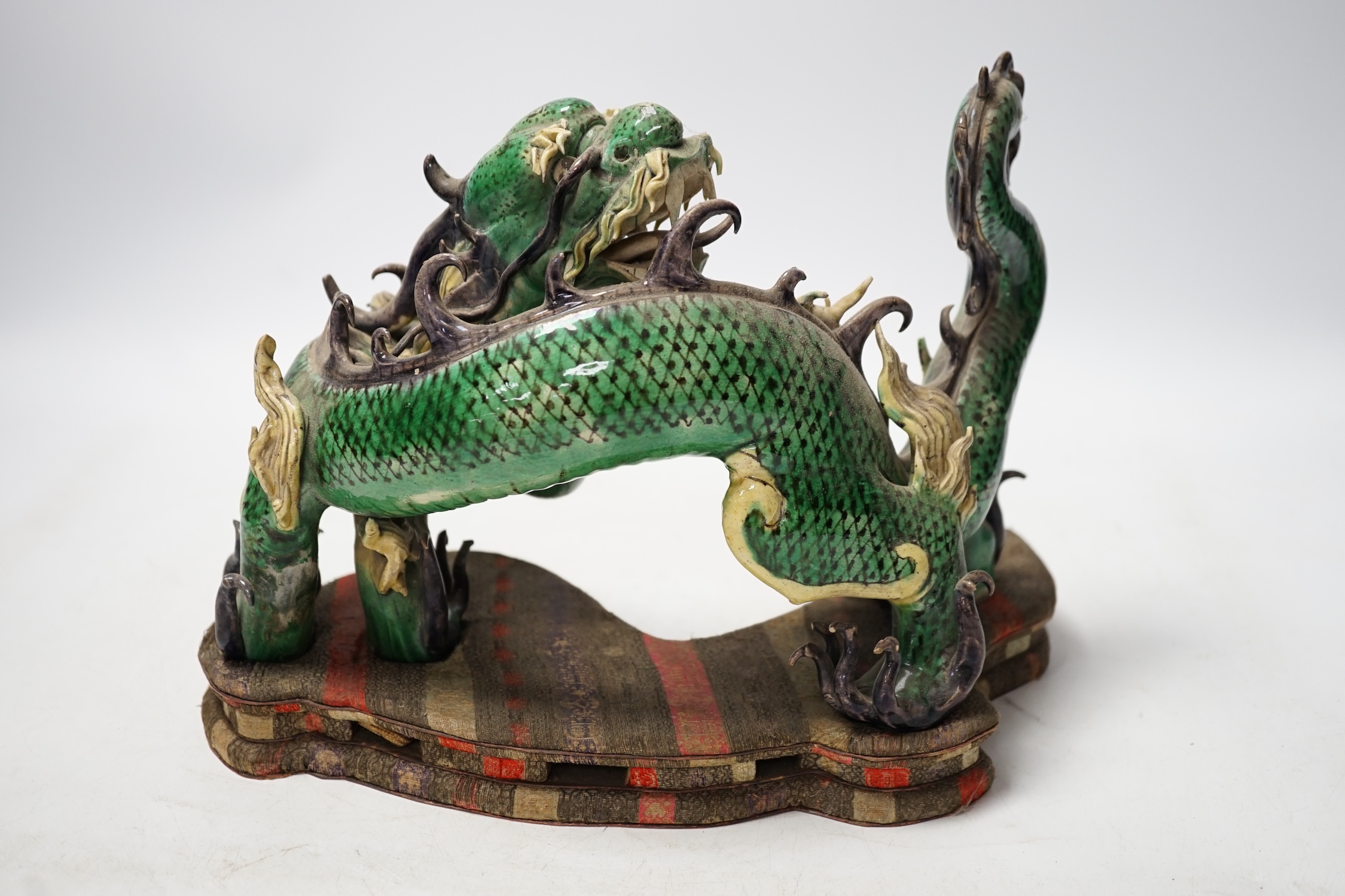 A Chinese sancai glazed model of a dragon, silk covered stand, 28cm wide. Condition - some damage